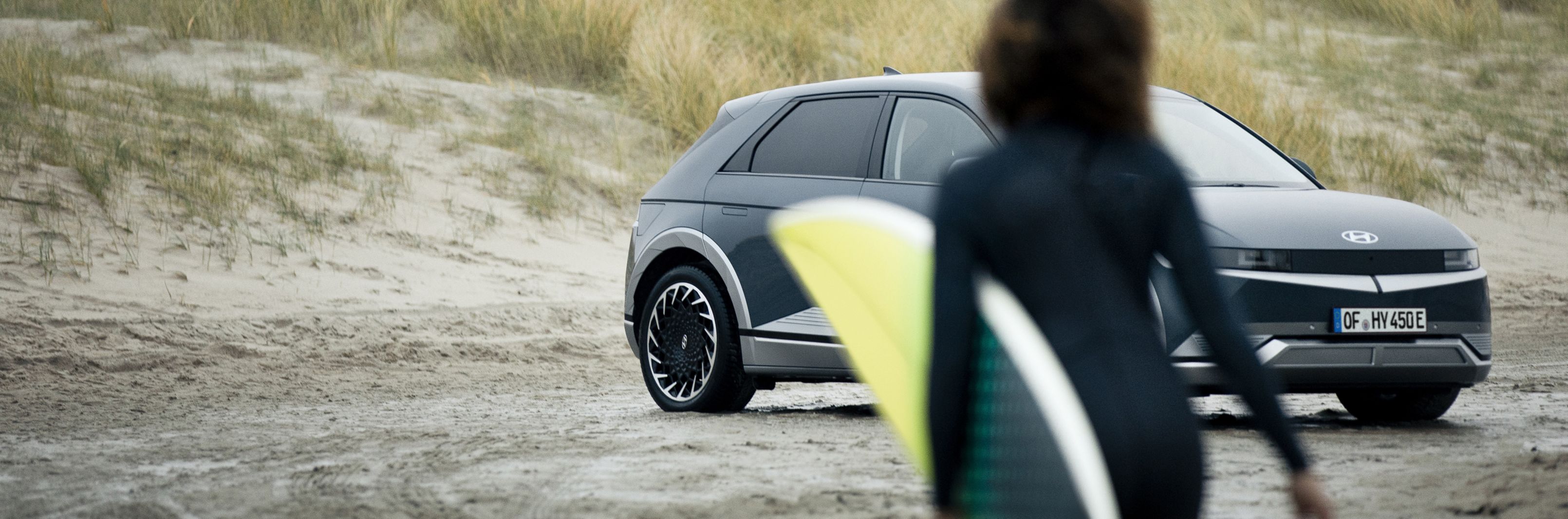 A surfer approaching her Hyundai IONIQ 5 electric vehicle parked on the beach.