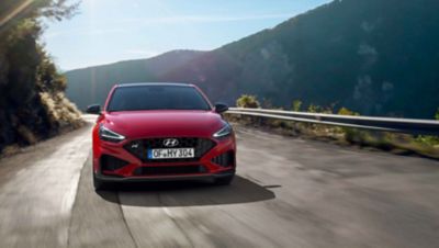 The new Hyundai i30 N driving in a hilly set in the colour Engine Red.