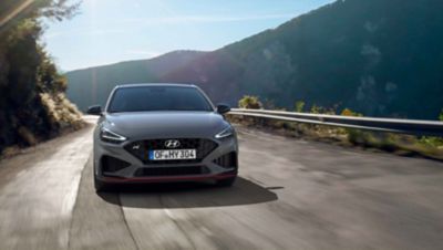 The new Hyundai i30 N driving in a hilly set in the colour Shadow Grey.