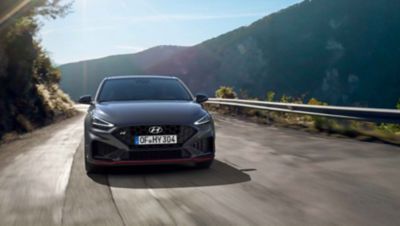 The new Hyundai i30 N driving in a hilly set in the colour Dark Knight Pearl.