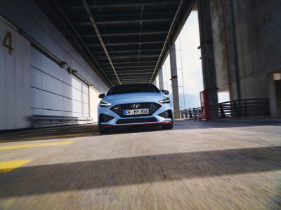 the new Hyundai i30 N from the front in Performance Blue colour driving along an industrial structure
