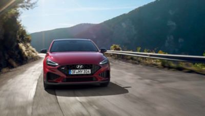 The new Hyundai i30 N driving in a hilly set in the colour Sunset Red.