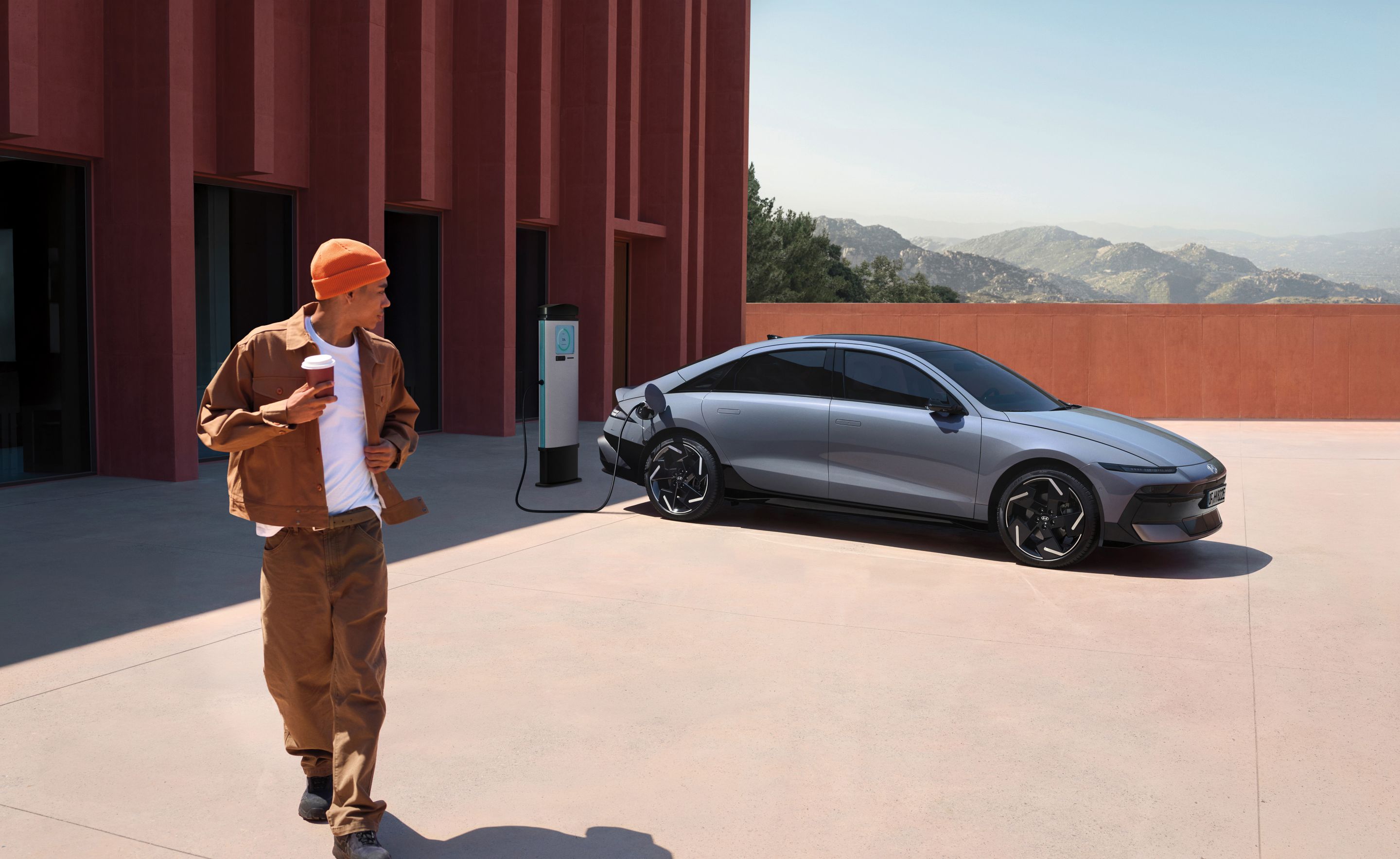 A man walking away from the Hyundai IONIQ 6 with a coffee cup while the car is plugged in to charge.
