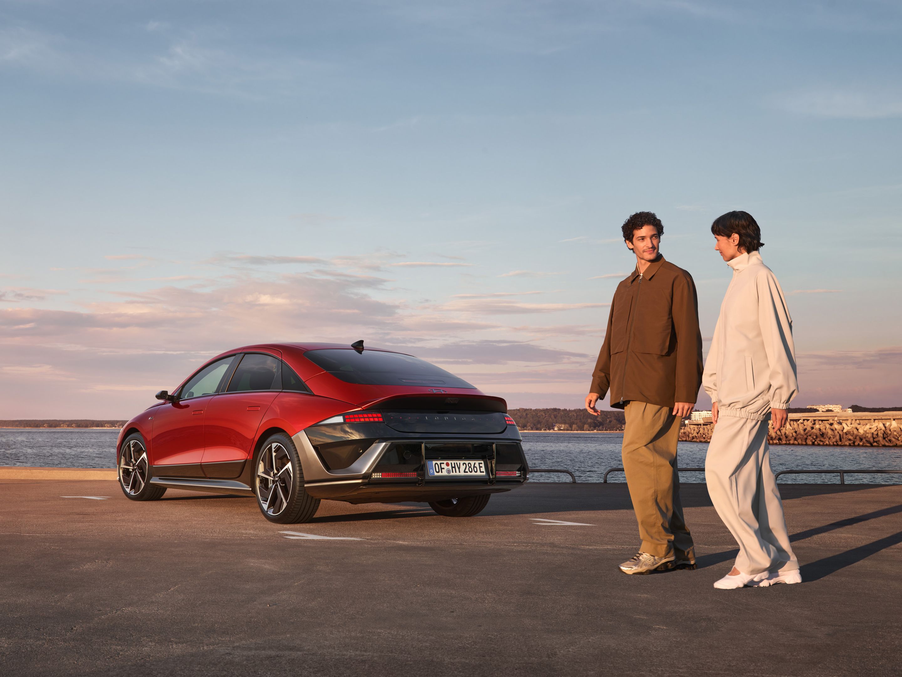 A man and woman walking past the rear of a Hyundai IONIQ 6 parked by the waterfront.