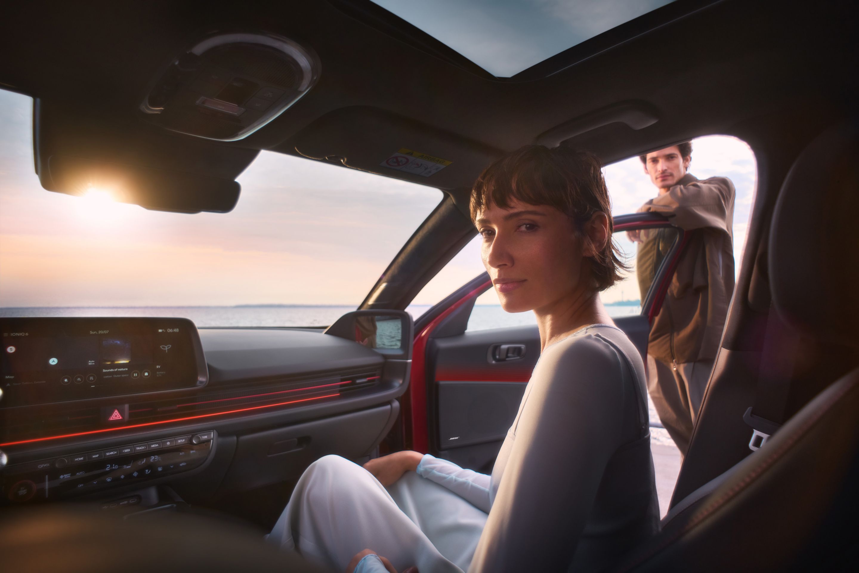 A woman in the front passenger seat of the Hyundai IONIQ 6 with a man leaning on the open door.