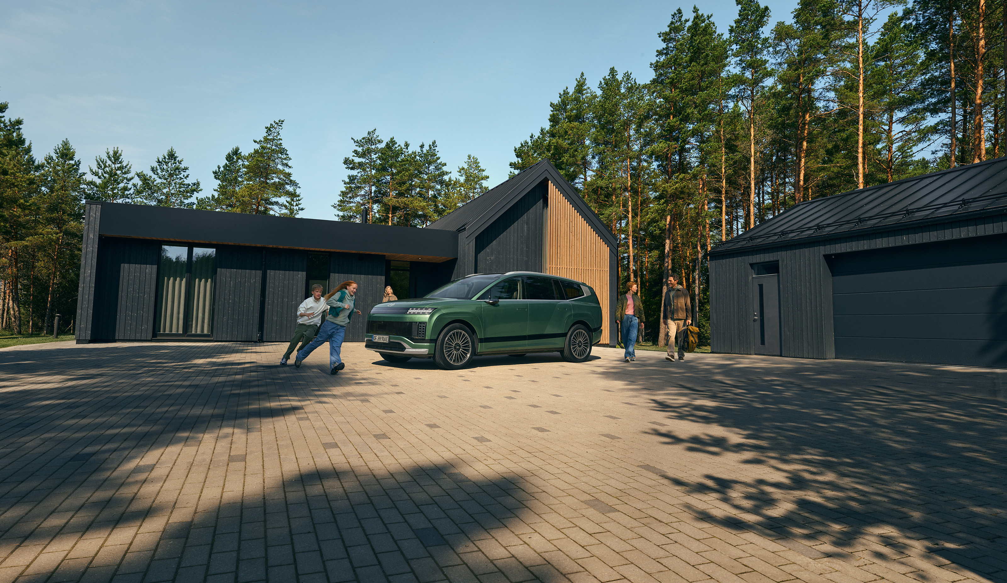 Side view of the Hyundai IONIQ 9 electric SUV with kids running around it in front of a house.	