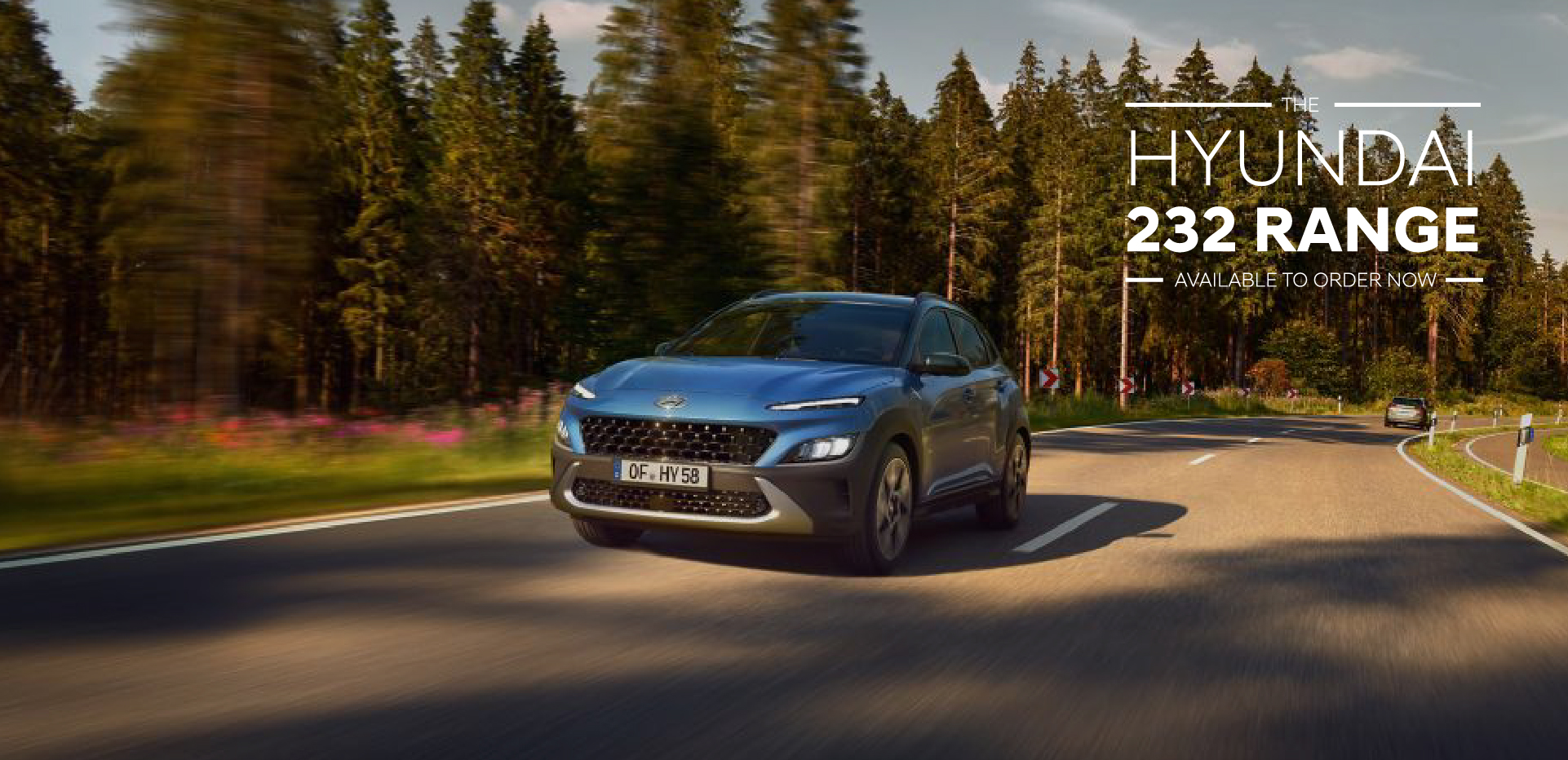The new Hyundai Kona from the front in Surfy Blue driving down a forest road.