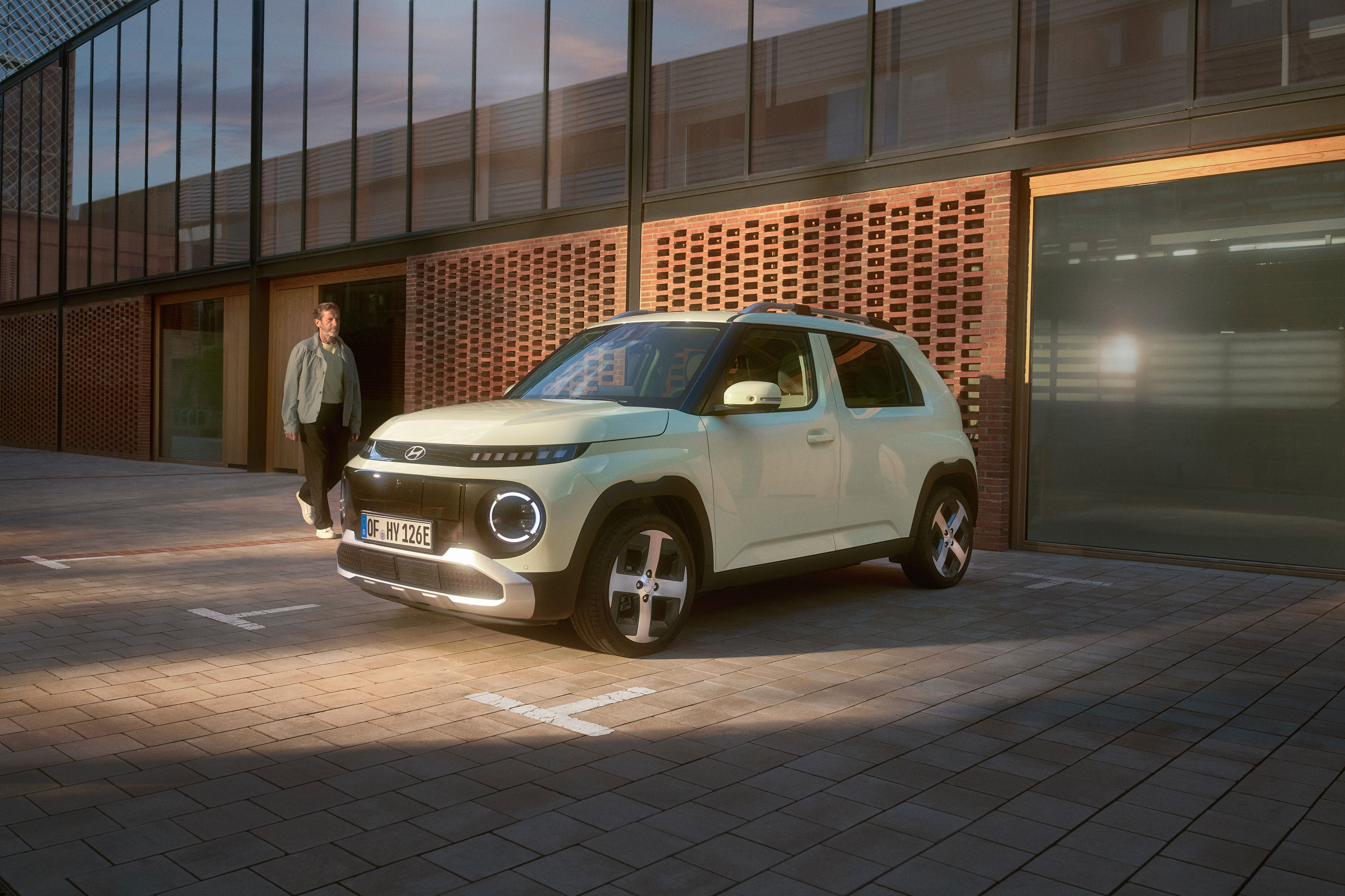 Hyundai INSTER parked in a courtyard as a person approaches from a doorway in soft evening light.