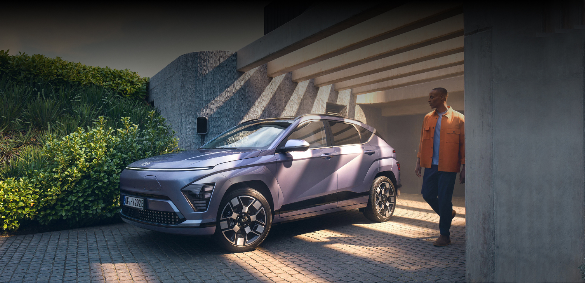 The Hyundai KONA Electric bathed in sunlight with a man walking away from a garage.