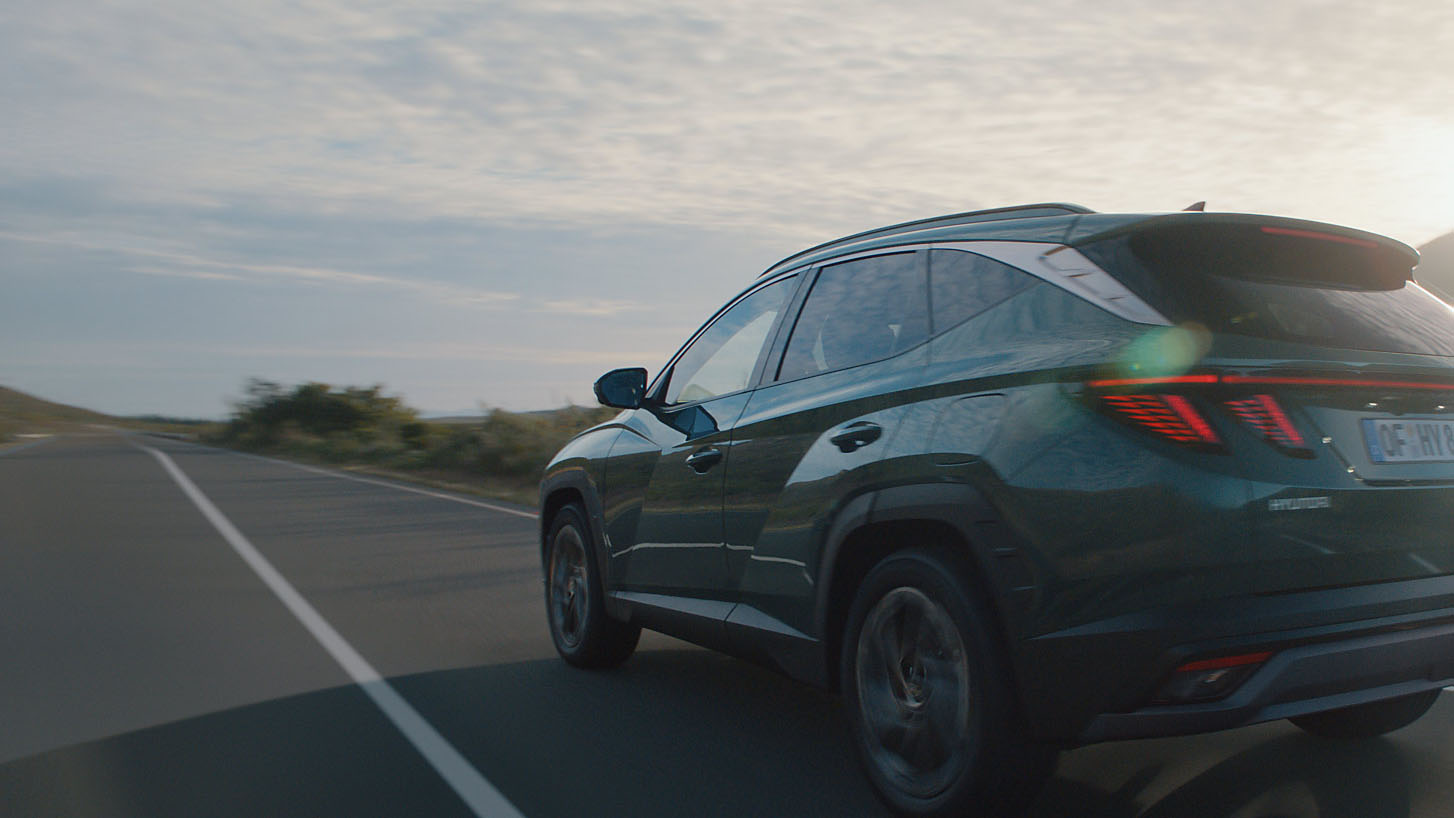 A blue Hyundai TUCSON Hybrid driving down a long, empty street.