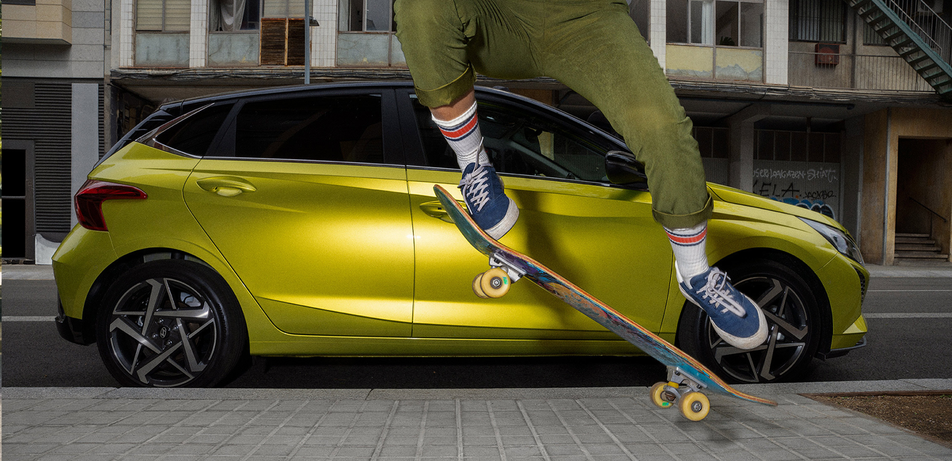 A young woman skateboarding in the street with a Hyundai i20 in the background.