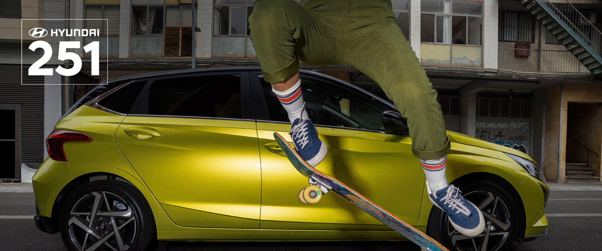 A young woman skateboarding in the street with a Hyundai i20 in the background.	