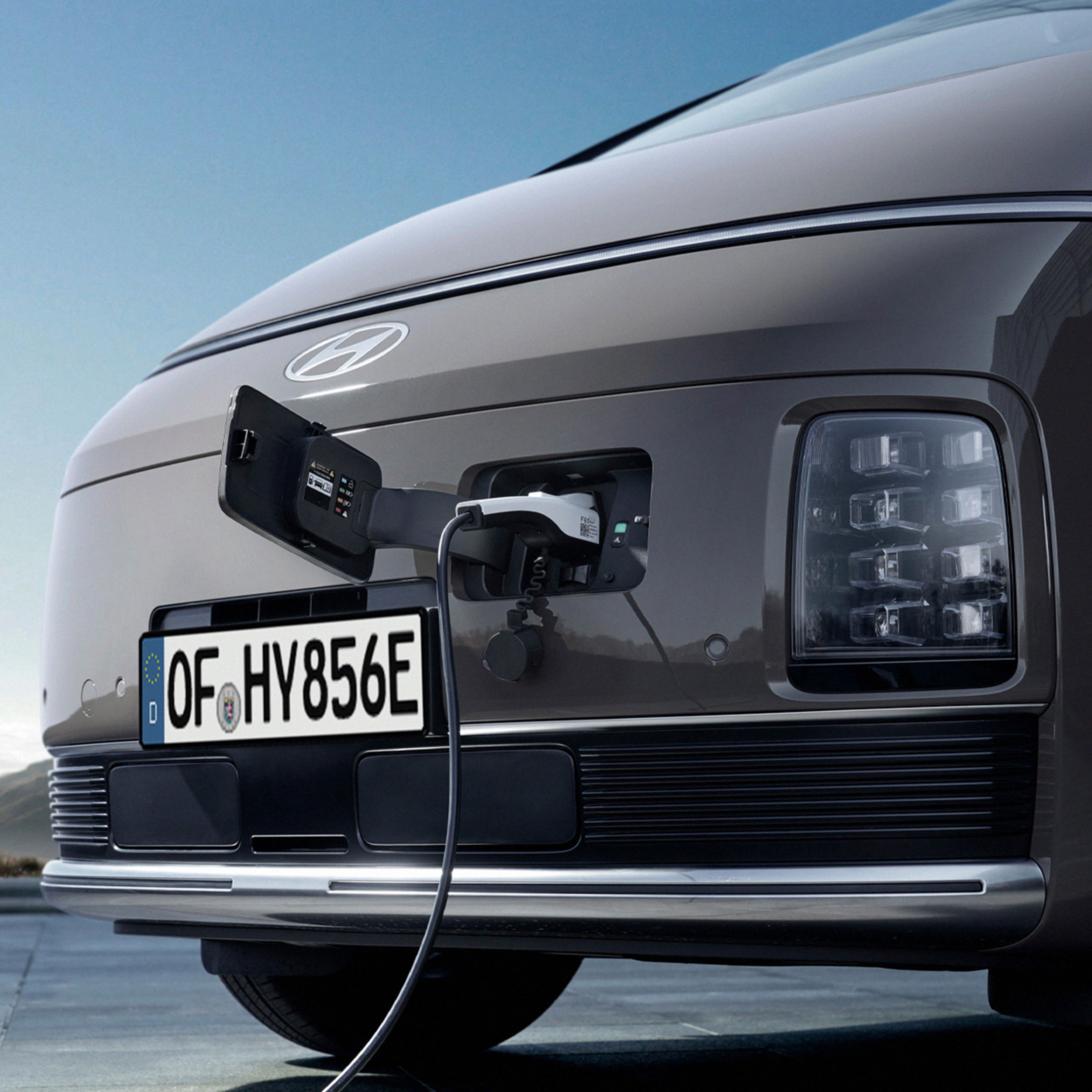 Close-up of the Hyundai STARIA Electric front end with open charging port and plugged-in charging cable.