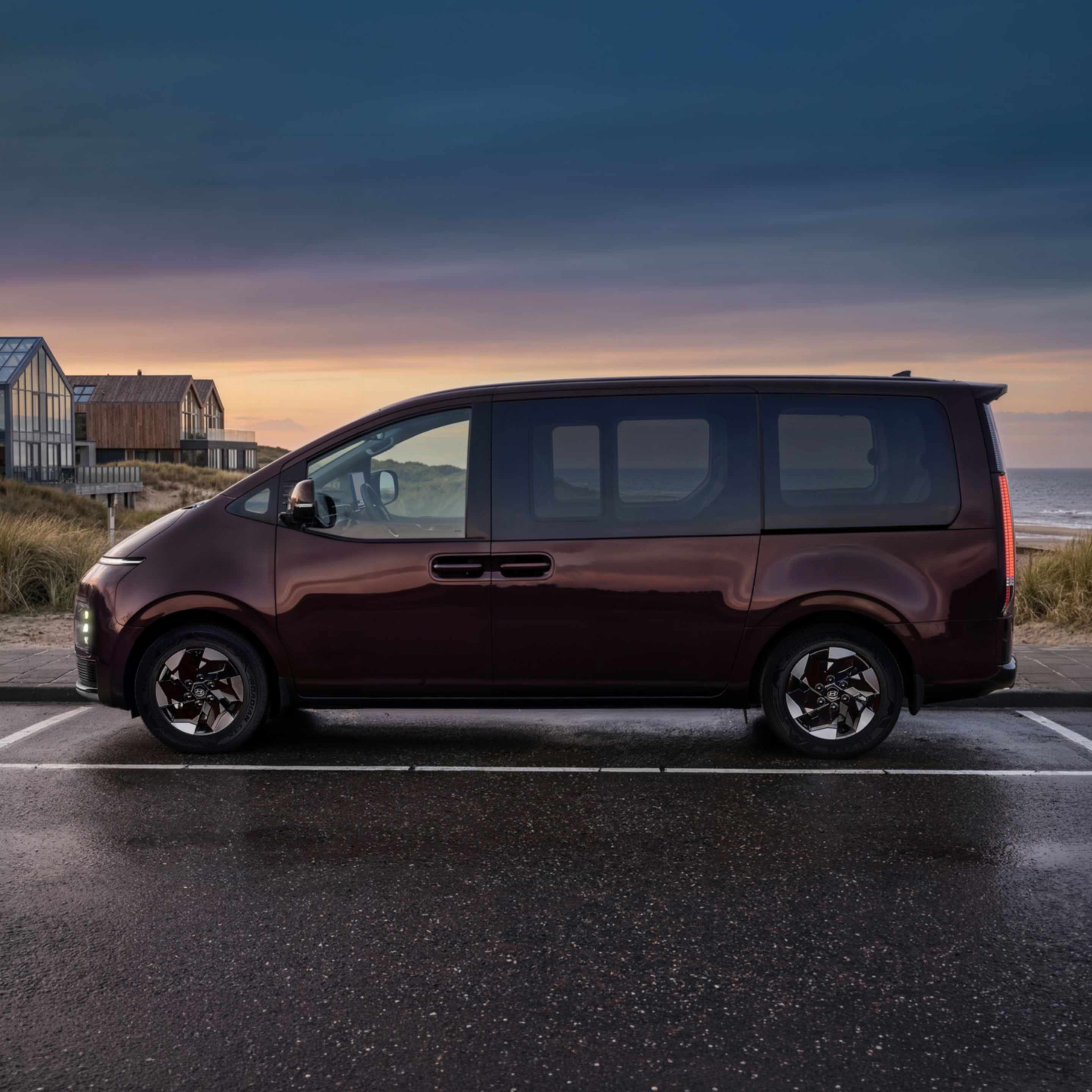 Side profile of the Hyundai STARIA Electric parked by the ocean at dusk.