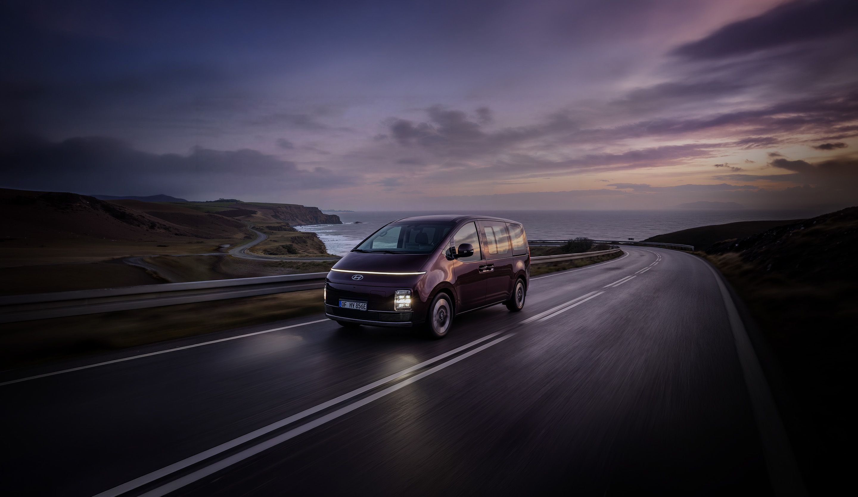 Hyundai STARIA Electric driving along a coastal road at sunset.