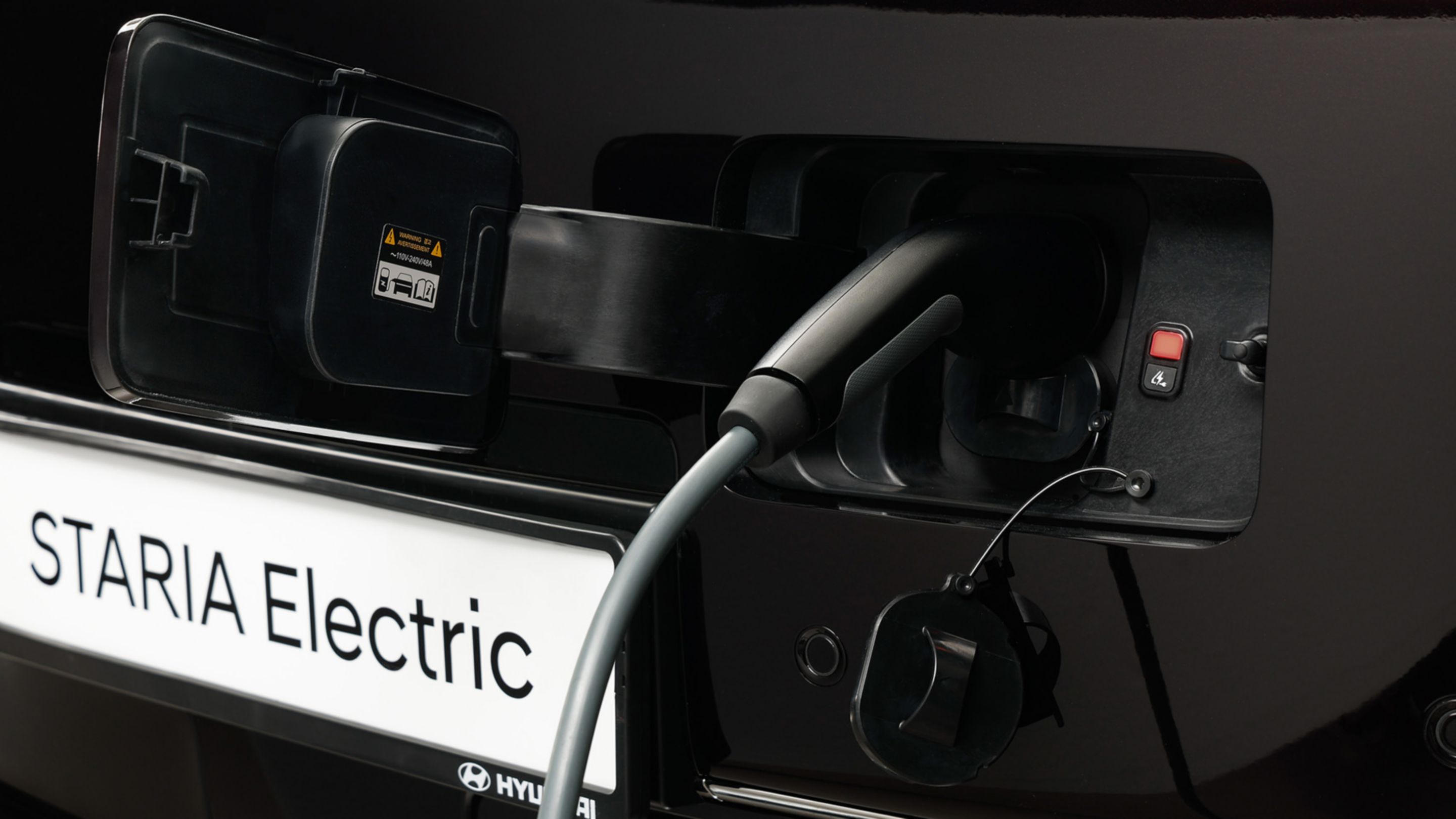 Close-up of the STARIA Electric charging port with cable connected for electric charging.