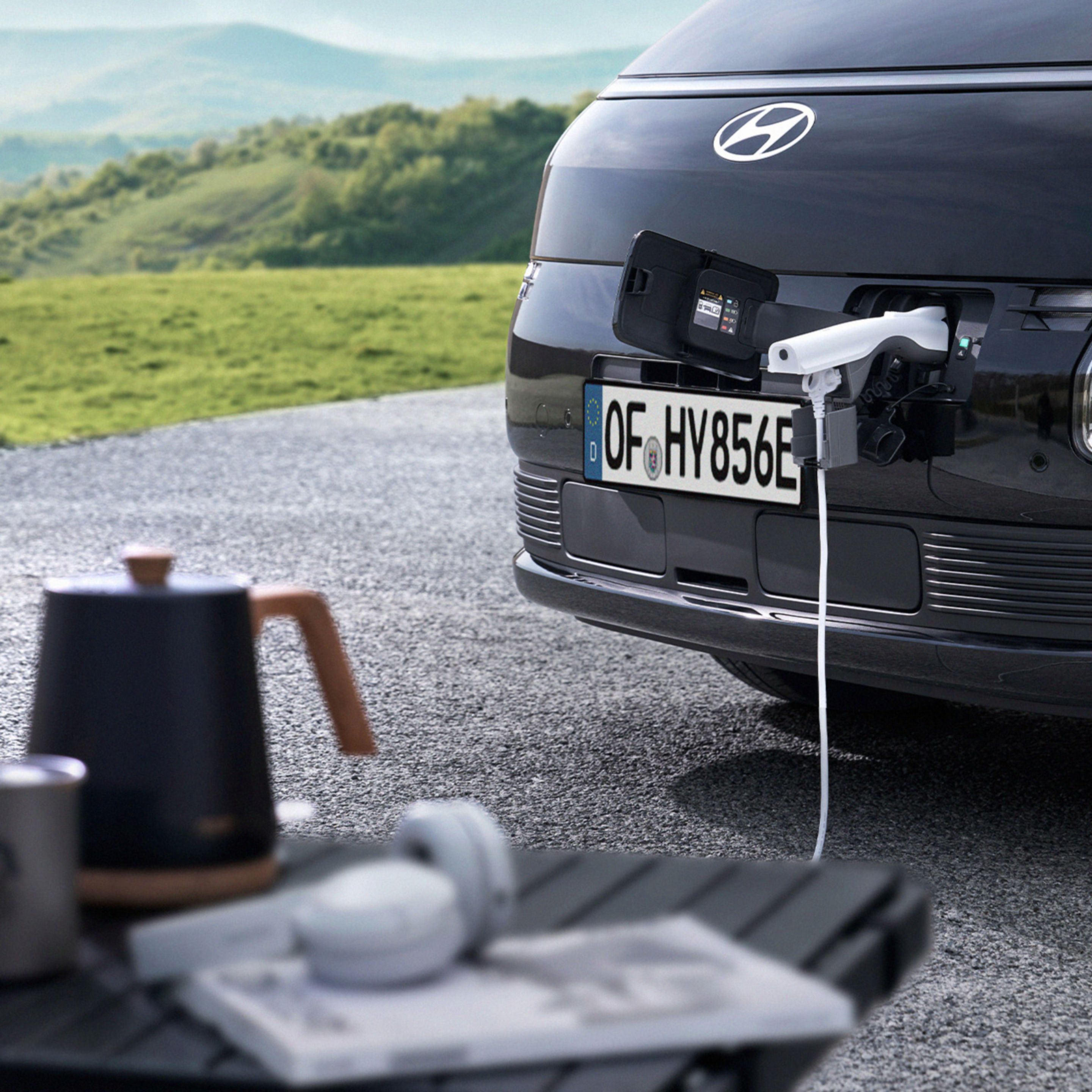 Hyundai STARIA Electric front charging port supplying power to an external device using Vehicle-to-Load (V2L) functionality.