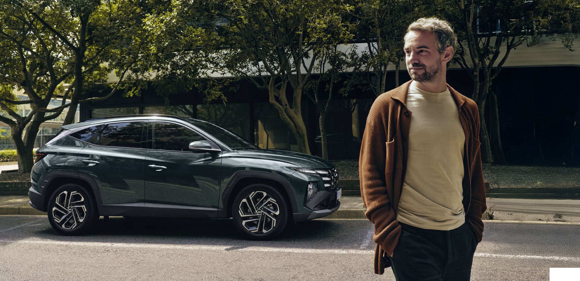 A man walking near a Hyundai&nbsp;TUCSON Hybrid parked by some trees.