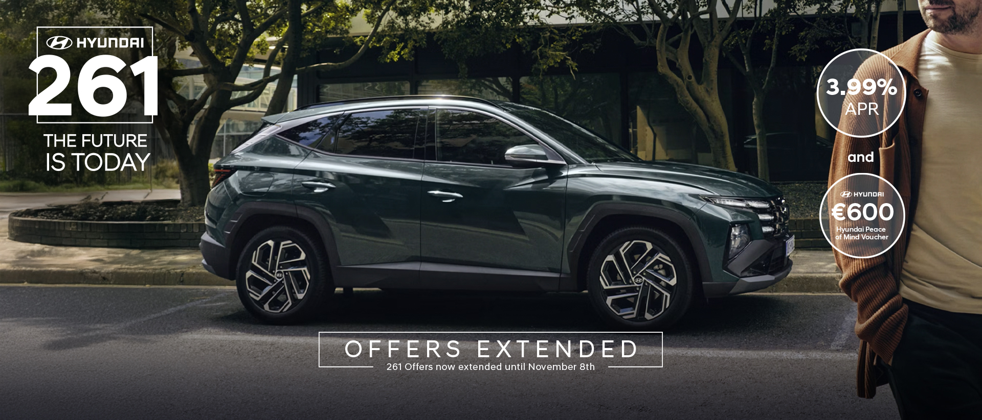 A man walking near a Hyundai TUCSON Hybrid parked by some trees.