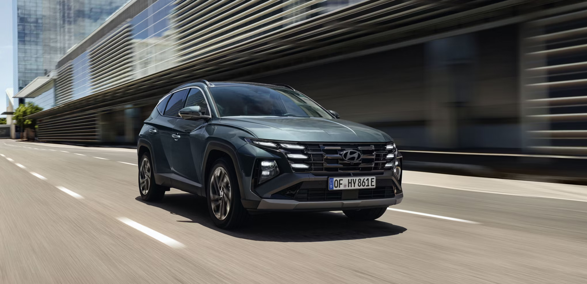 The Hyundai TUCSON Plug-in Hybrid driving down a city street with modern buildings visible.